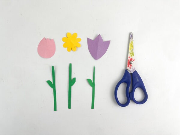 Cut-out paper flower shapes and stems in pink, yellow, purple, and green next to a pair of scissors.