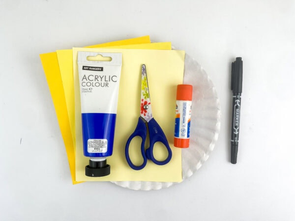 Craft supplies including yellow paper, a white paper plate, blue paint, scissors, a glue stick, and a black marker.