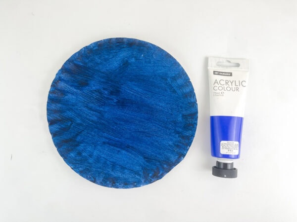 A paper plate painted solid blue next to a tube of blue acrylic paint.