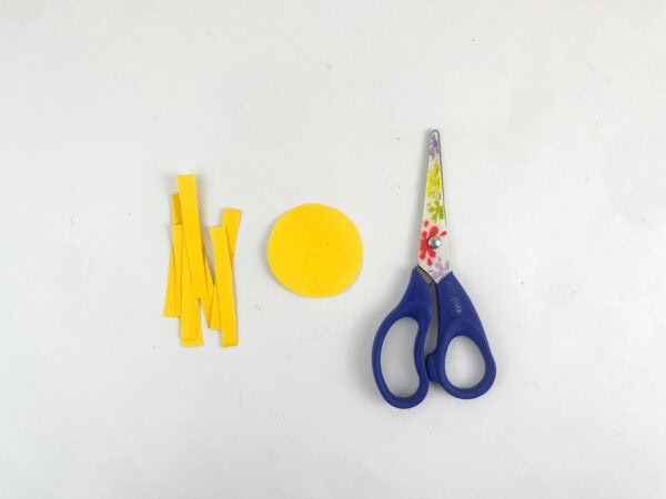 Cut-out yellow paper strips and a circle next to blue scissors.