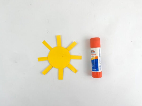 An assembled yellow paper sun next to an orange glue stick.