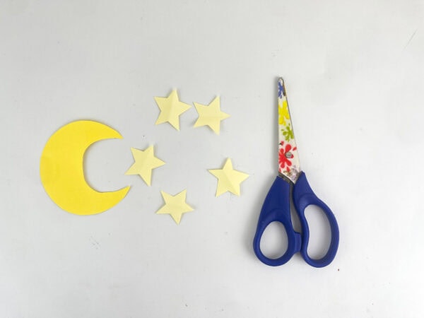 A cut-out yellow paper crescent moon and five small stars next to scissors.