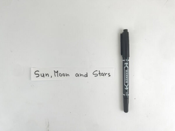 A white paper strip with the handwritten words "Sun, Moon and Stars" next to a black marker.
