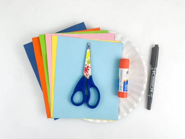 Craft supplies including multi-colored construction paper, scissors, a glue stick, a black marker, and a paper plate.