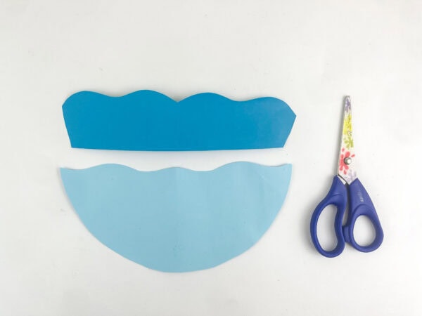 Two blue paper cutouts shaped like waves next to a pair of scissors.