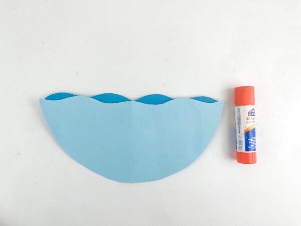 Two different shades of blue paper waves glued together next to a glue stick.