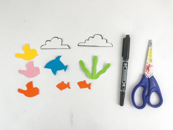 Colorful paper cutouts of birds, clouds, fish, and seaweed arranged next to a black marker and scissors.