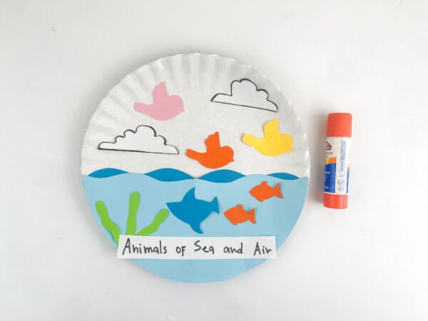 Finished paper plate craft with the "Animals of Sea and Air" label attached at the bottom next to a glue stick.