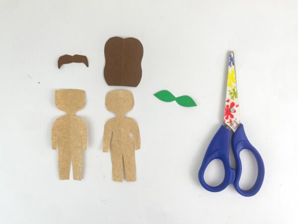 Cut-out brown paper human figures and hair pieces next to a pair of scissors.
