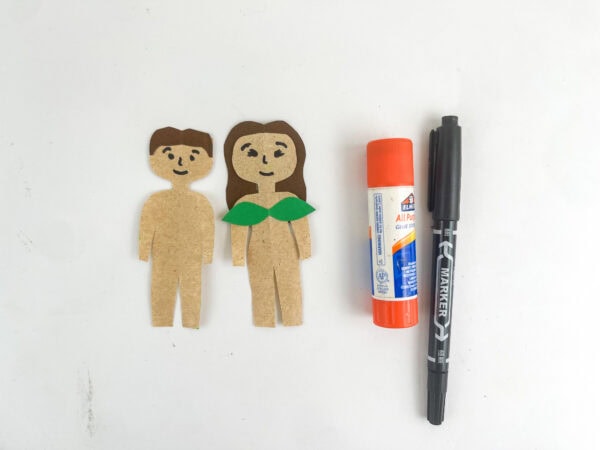 Cut-out paper figures of a man and woman with faces drawn on, next to a glue stick and a black marker.