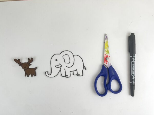 Cut-out paper figures of a deer and an elephant next to a pair of scissors and a black marker.