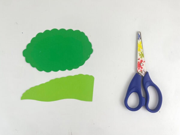 Cut-out pieces of green construction paper next to a pair of scissors.