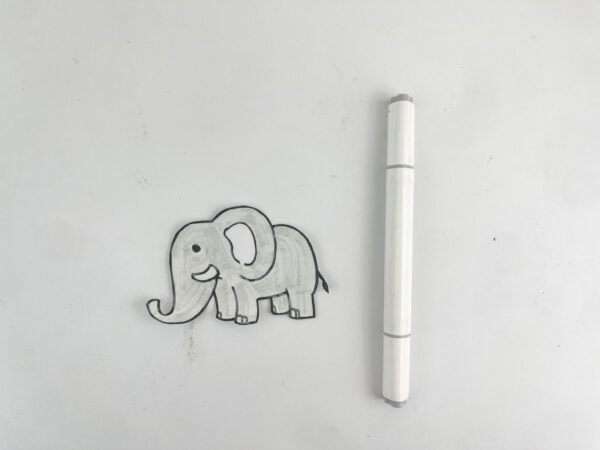 A cut-out paper drawing of an elephant next to a grey marker.