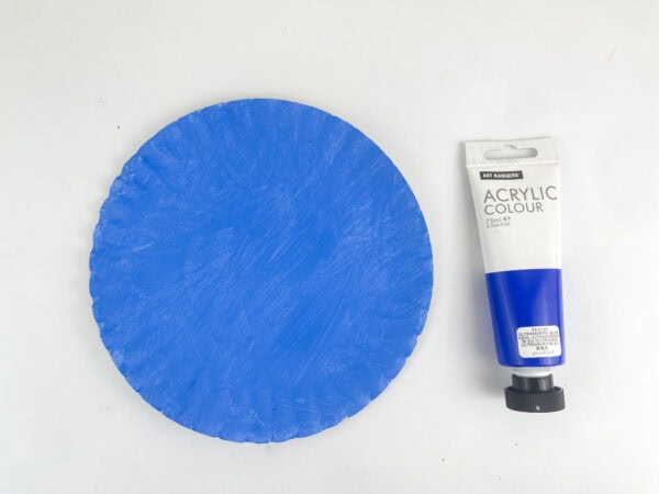 A paper plate painted completely blue next to a tube of blue acrylic paint.