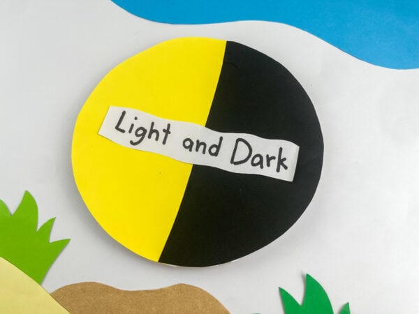 A close-up view of the completed "Light and Dark" circle craft resting on paper cutout hills and grass.