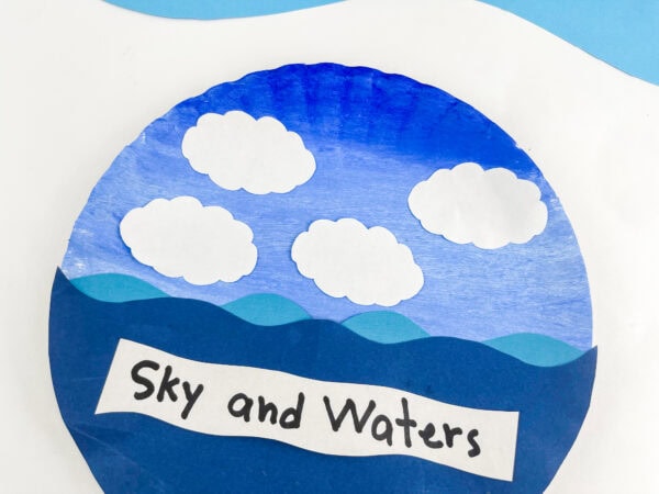A close-up view focusing on the upper half of the finished paper plate craft, showcasing the four cloud cutouts and the "Sky and Waters" label.