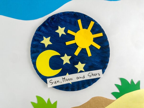 Completed paper plate craft featuring a yellow sun, crescent moon, and stars on a blue background.
