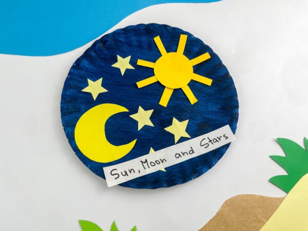 The finished paper plate space craft placed on a decorative background with blue and green paper cut-outs.