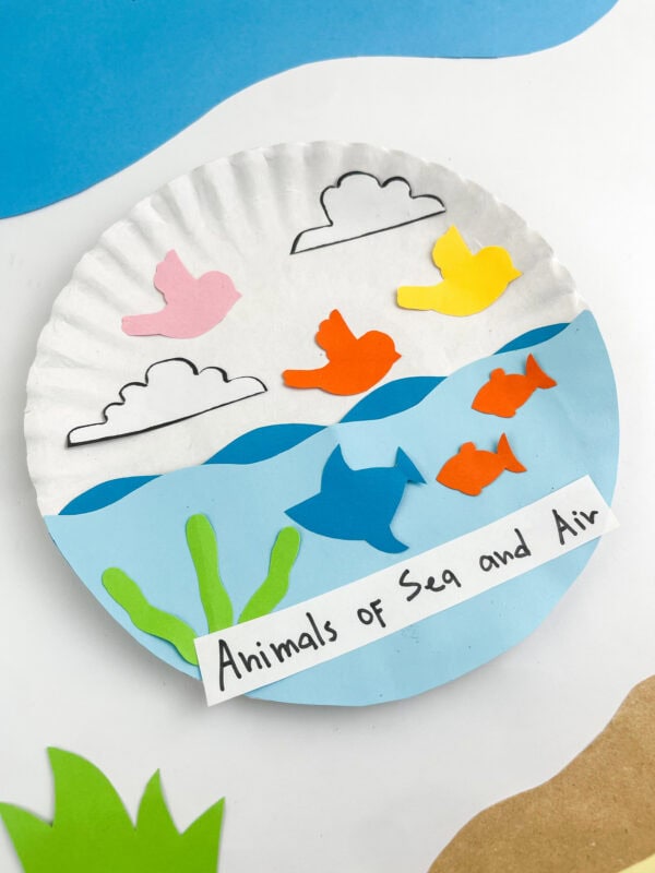 A close-up view of the finished paper plate craft highlighting the vibrant bird, cloud, fish, and seaweed paper cutouts.
