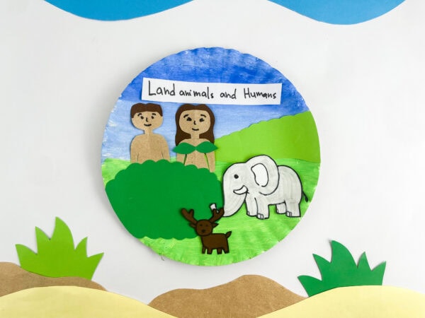 A completed paper plate craft depicting Adam, Eve, an elephant, and a deer with a label that reads "Land animals and Humans."