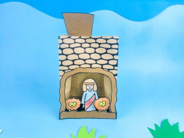  Finished paper bag craft showing Daniel in a cave with two lions, against a blue sky background.