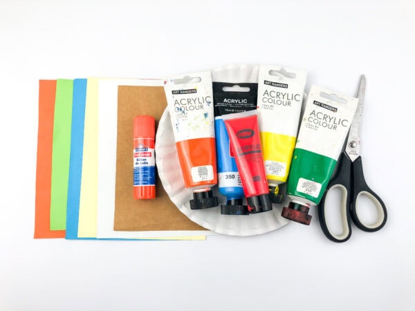Craft supplies laid out: colored paper sheets, a paper plate, glue stick, acrylic paint tubes, and scissors.