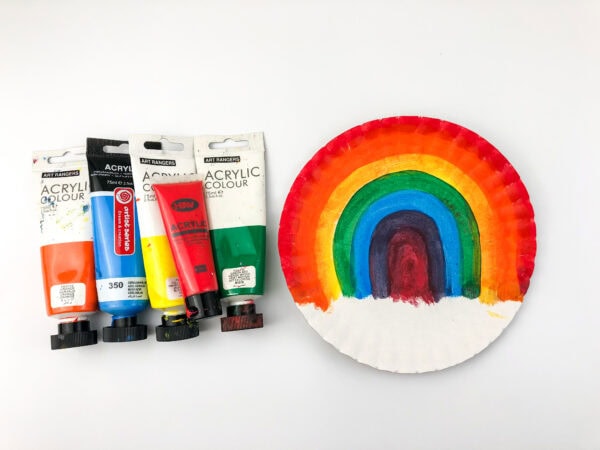 Paint tubes beside a paper plate painted with a rainbow design.