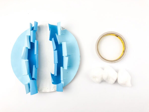 The standing wave-shaped paper circle next to a roll of tape and three cotton balls.
