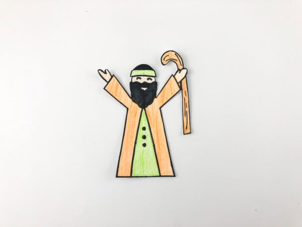 The same paper figure now colored in with an orange robe, green undershirt, and brown staff.