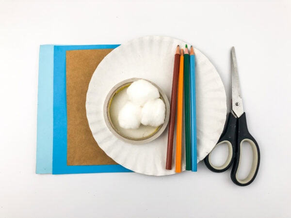 Craft supplies laid out: blue and light blue paper, brown paper, a paper plate, cotton balls in a bowl, colored pencils, and scissors.
