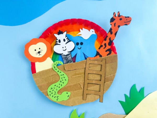 Close-up of completed Noah's Ark paper plate craft showing rainbow background and animal cutouts peeking over a cardboard ark.