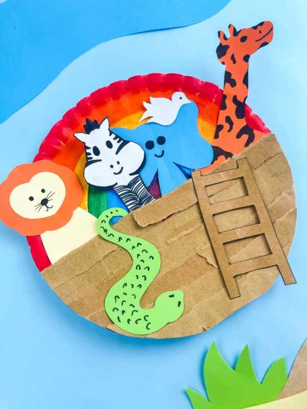 completed Noah's Ark paper plate with rainbow above and layered cardboard hull planks below

