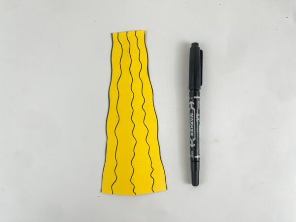 drawing wavy black marker detail lines on yellow fabric panel for King Solomon paper bag puppet craft