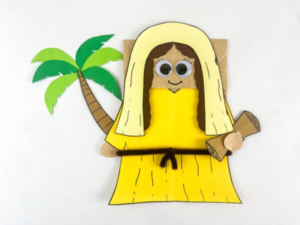 Deborah paper bag puppet with googly eyes and smile drawn nearly complete with palm tree beside her