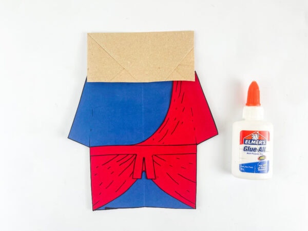 assembling Ezekiel paper bag puppet body with blue robe red sash and belt on kraft paper bag