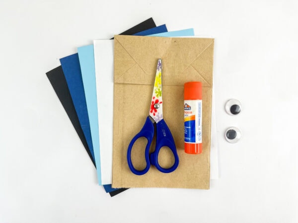 Craft supplies with paper bag, scissors, glue stick, and paper.