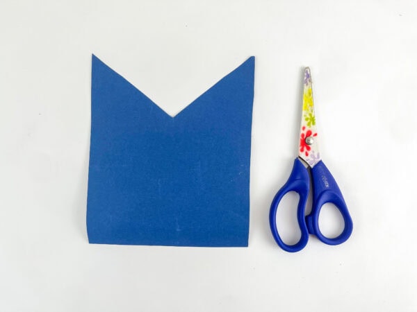 Blue paper bag cut into a shirt shape beside scissors.