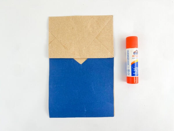 Folded paper bag with blue shirt and glue stick.