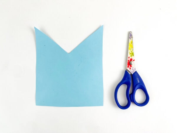 Blue paper bag cut into a shirt shape beside scissors.