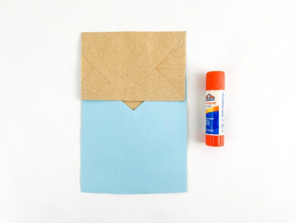 Folded paper bag with blue shirt and glue stick.