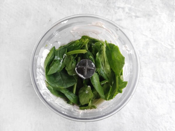 Fresh spinach leaves in a small blender with cream cheese mixture.