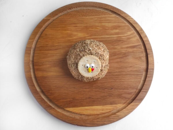 Nut-coated turkey cheese ball with a round cracker face and candy eyes