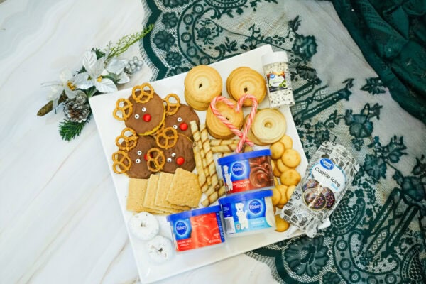 Assorted cookies, pretzels, wafers, candy canes, and frosting containers arranged on a white platter for a reindeer dessert board.