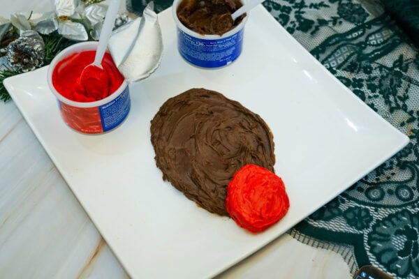 Chocolate frosting shaped into Rudolph's face with a large round red frosting nose at the bottom.