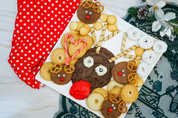 Completed Christmas reindeer frosting board with wafer antlers, mini Rudolph cookies, powdered doughnuts, pretzels, and candy canes.