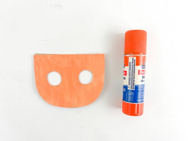 Painted elf face with eye holes beside a glue stick.