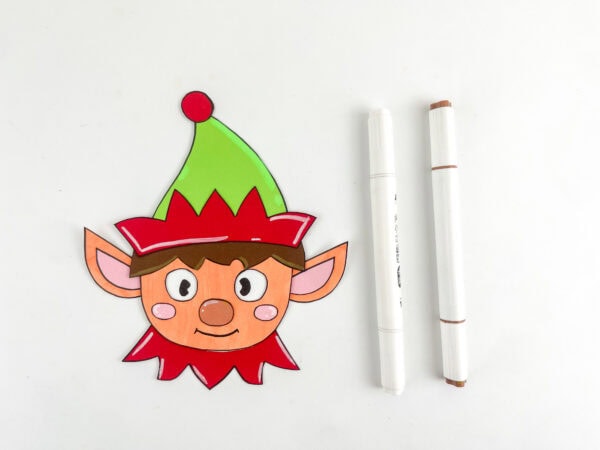 Finished elf face with drawn eyes and markers beside it.